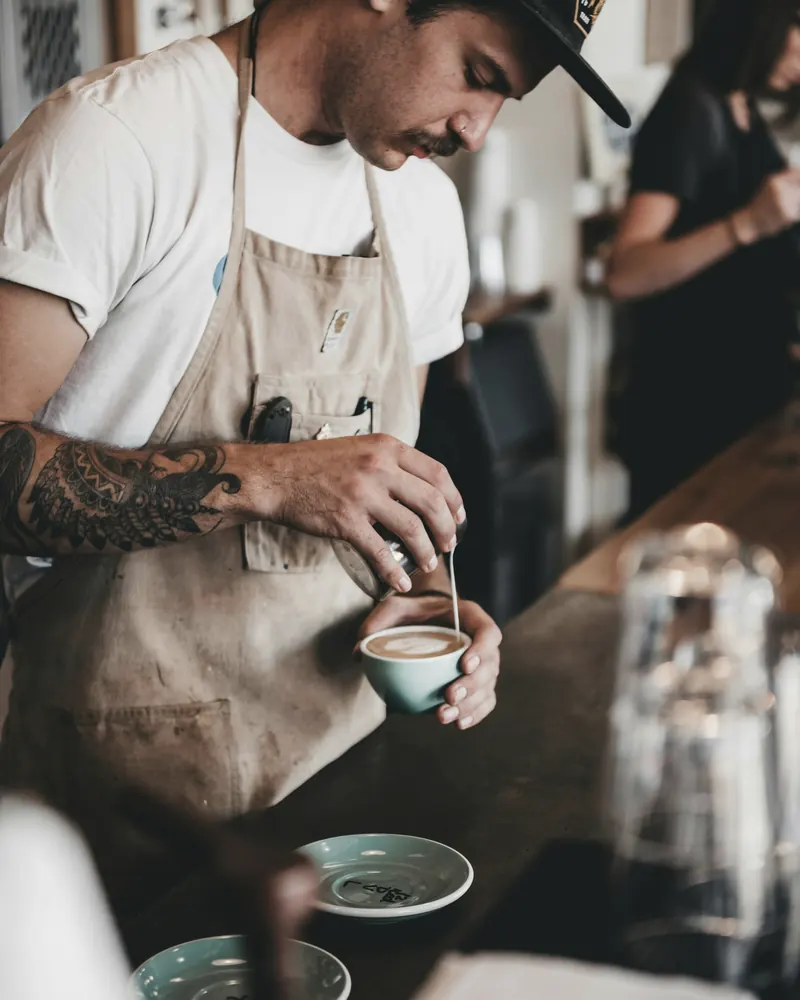 A barista pouring latte art behind a cafe counter